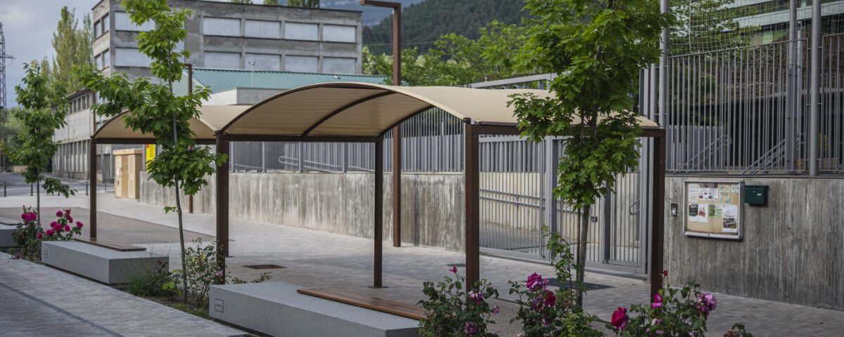 Pérgola exterior de estructura metálica con cubierta textil en una zona ajardinada