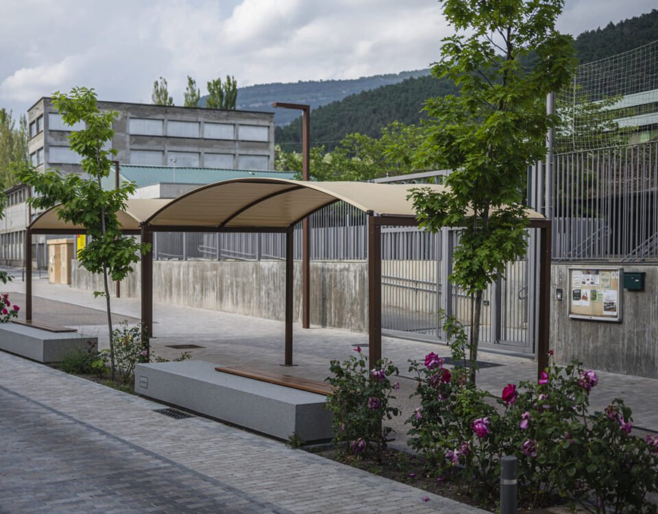 Pérgola exterior de estructura metálica con cubierta textil en una zona ajardinada